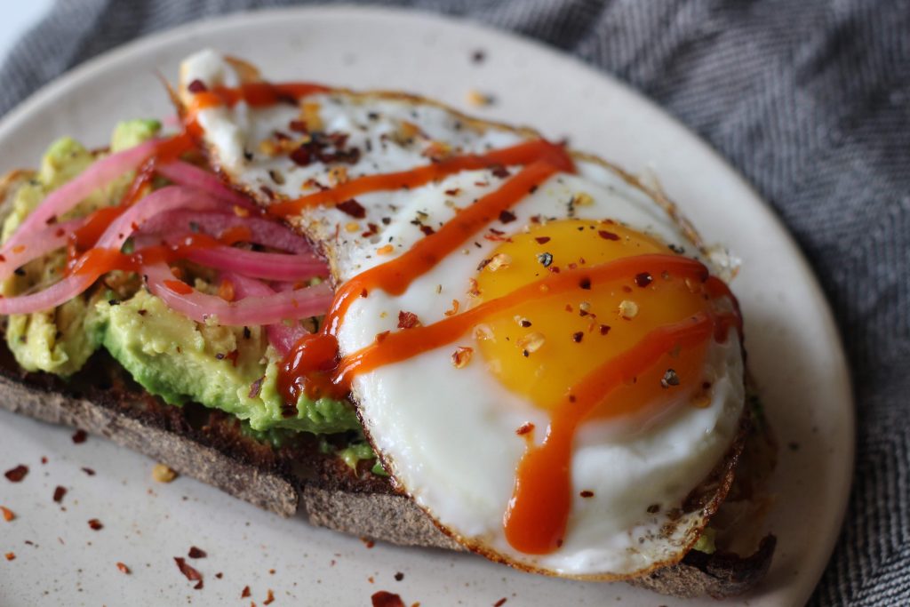 sourdough toast with avocado, pickled onions, and egg on top. topped with crushed red peper.