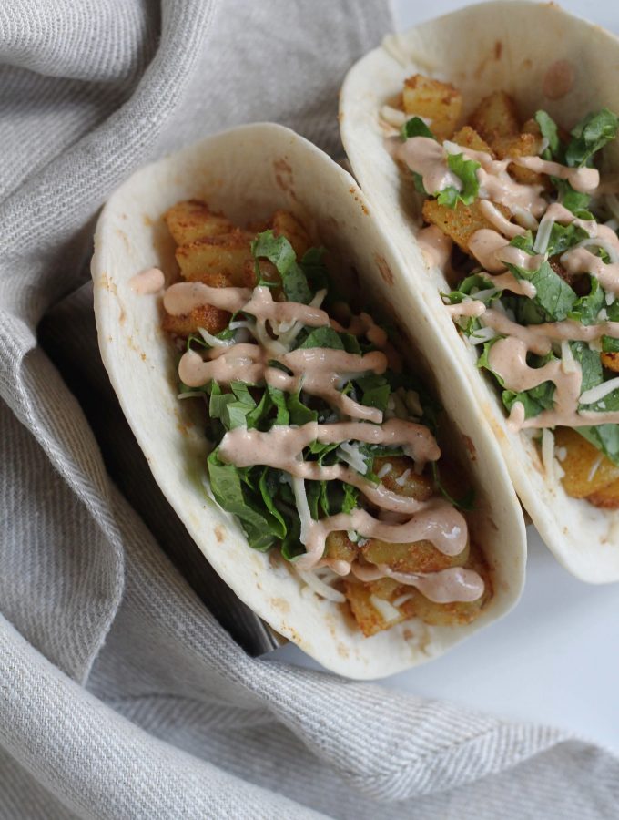 Flour tacos with diced potatoes, lettuce and chipotle sauce on them.
